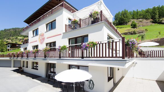 A modern building with a balcony, adorned with flowers. In the background, green hills and a blue sky can be seen. - Haus PIA by A CASA - Sölden