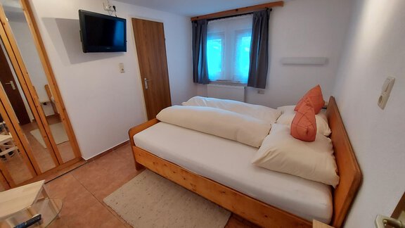 A cozy bedroom with a double bed and two pillows. There is a television and large windows that let in light. - Haus Pitzwald - Sölden
