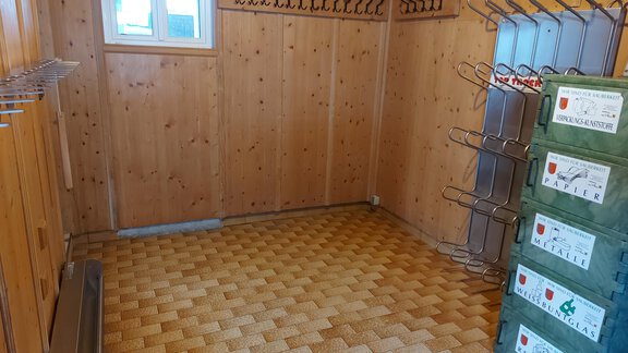 An empty room with wooden walls and a window. On the wall, there are coat hooks and stacked boxes. - Haus Pitzwald - Sölden