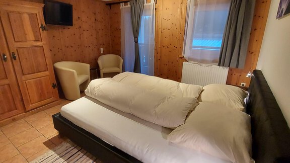 A cozy bedroom with a double bed and a television on the wall. The walls are made of wood, and there is an armchair as well as a wardrobe. - Haus Pitzwald - Sölden