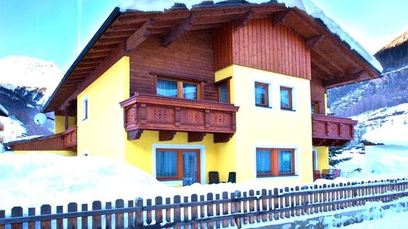 A charming wooden house with a yellow facade and balcony, surrounded by snow-covered landscapes. It is situated in the mountains and exudes a cozy atmosphere. - Haus Romana - Sölden