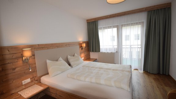 A modern bedroom with wooden accents and a large window. There is a double bed with white bedding and a cozy armchair. - Haus Romana - Sölden