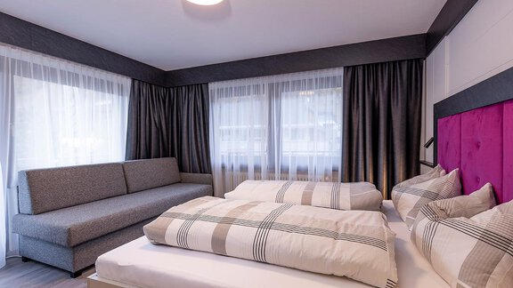 A modern bedroom with two beds and a gray sofa. Large windows provide plenty of natural light. - Haus Sieglinde Color - Sölden