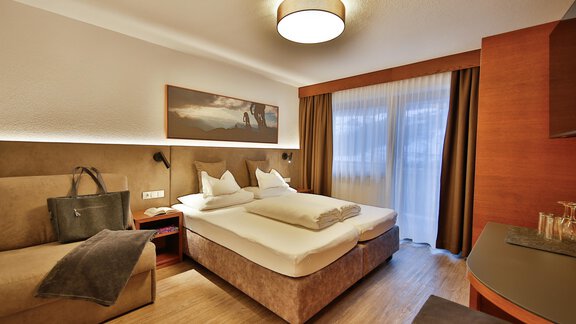 A modern hotel room with a double bed and a cozy sofa. Large windows provide plenty of daylight and an inviting atmosphere. - Haus Söldenblick - Sölden