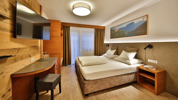 A modern hotel room with two beds and light-colored walls. There is a flat-screen TV and a window with curtains. - Haus Söldenblick - Sölden