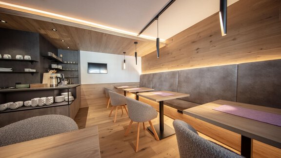 A modern café with light wooden furniture and cozy tables. The warm lighting creates an inviting atmosphere. - Haus Sonnwend - Sölden
