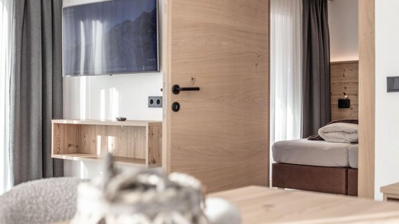 A modern room with wooden details and a TV on the wall. In the background, a bed can be seen, while the room looks bright and inviting. - Haus Sonnwend - Sölden