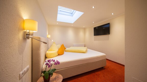 A bright bedroom with a large bed and colorful cushions. There is a television on the wall and a window that lets light in. - Haus Stefanie - Sölden