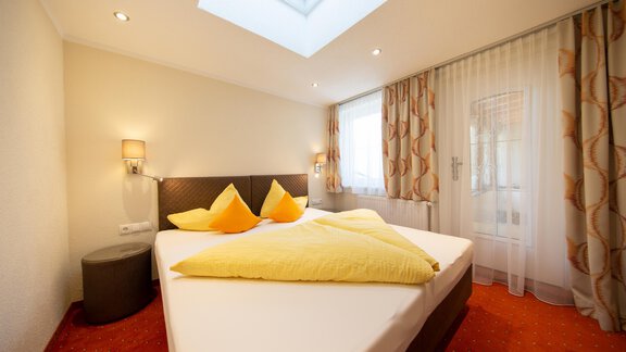 A bright bedroom with a large bed and colorful pillows. The room has large windows and a cozy atmosphere. - Haus Stefanie - Sölden