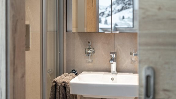 A modern bathroom with a white sink and a large mirror. In the background, mountains are visible, and a towel hangs decoratively on the wall. - Haus Ulrich - Sölden