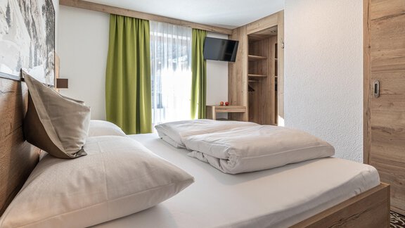 A modern bedroom with a large bed and pillows. The green curtains and natural wood give the room a cozy atmosphere. - Haus Ulrich - Sölden