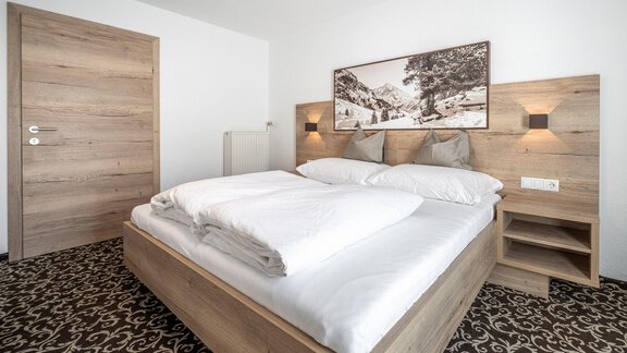 A cozy bedroom with a large double bed and modern wood design. The walls are light and there are artworks depicting a mountainous landscape. - Haus Ulrich - Sölden
