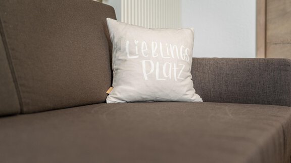 A cozy sofa with a cushion that says "Favorite Spot." The colors are neutral and inviting. - Haus Ulrich - Sölden