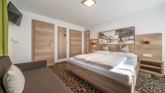 A modern bedroom with a double bed and a cozy couch. The walls are bright, and there is beautiful decoration with a landscape picture. - Haus Ulrich - Sölden