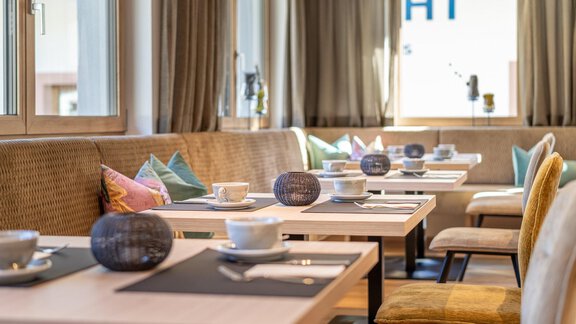 A cozy restaurant atmosphere with bright tables and comfortable seating. Coffee cups and decorative elements are on the tables. - Haus Ulrich - Sölden