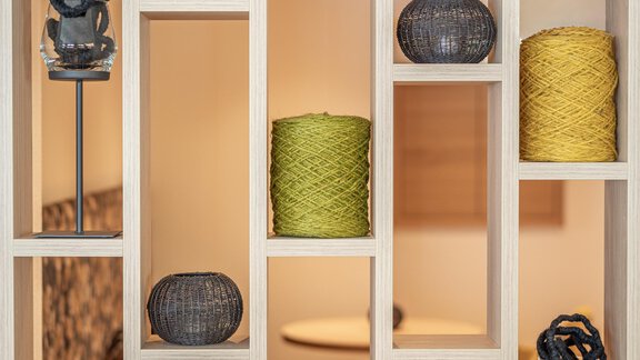 A modernly designed shelf with various decorative objects and colorful spools of thread. The background is light and friendly, creating a pleasant atmosphere. - Haus Ulrich - Sölden