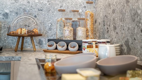 An inviting breakfast station with various cereals and jam in decorative jars. On the counter, there are plates and bowls prepared for a meal. - Haus Ulrich - Sölden
