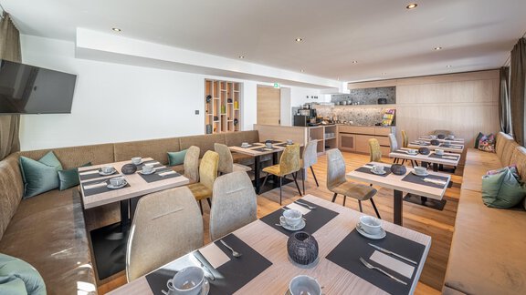 A modern restaurant with stylish tables and comfortable seating. The decor is bright and inviting, with an open kitchen in the background. - Haus Ulrich - Sölden