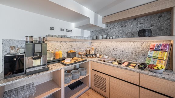 A modern kitchen with wooden shelves and an elegant stone surface. On the countertop, drinks, glasses, and various snacks are arranged. - Haus Ulrich - Sölden