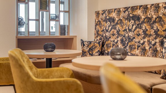 A modern café with patterned walls and cozy, yellow chairs. Round tables invite you to linger. - Haus Ulrich - Sölden