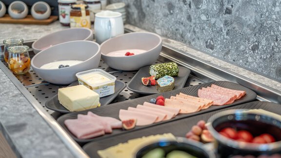 A breakfast buffet with various cold cuts, cheese, and fresh fruit. It includes bowls of yogurt and jam. - Haus Ulrich - Sölden