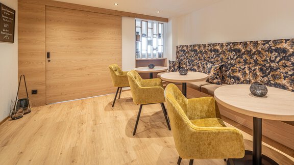 A modern café with bright wooden furniture and yellow chairs. There are round tables and a cozy atmosphere. - Haus Ulrich - Sölden