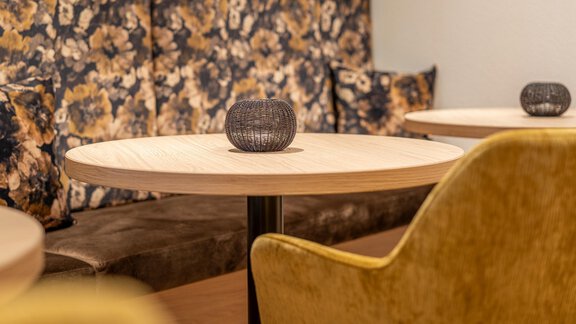 A cozy café with round wooden tables and comfortable yellow chairs. Decorative candle holders are placed on the tables. - Haus Ulrich - Sölden