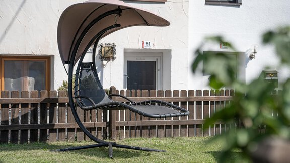 A cozy hammock chair with sun protection is in the garden. In the background, a fence and a house are visible. - Haus Valtelas - Sölden