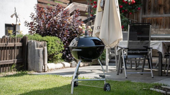 A black grill stands on a well-kept lawn in the garden. In the background, garden furniture and plants can be seen. - Haus Valtelas - Sölden