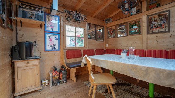 A cozy room with wooden walls and a long tablecloth. Pictures hang on the walls, and there is a seating area with red cushions. - Haus Valtelas - Sölden