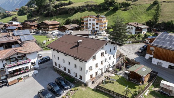 A picturesque mountain village view with several buildings and green terrain. Cars are parked in front of a white house, surrounded by nature. - Haus Valtelas - Sölden