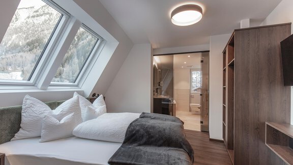 A modern bedroom with a cozy bed and large windows. The room has a clear, minimalist style and offers a view of nature. - Home4You - Sölden