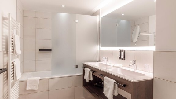 A modern bathroom with a bathtub and a separate shower. The room is bright and stylish, equipped with a large mirror and elegant fixtures. - Home4You - Sölden