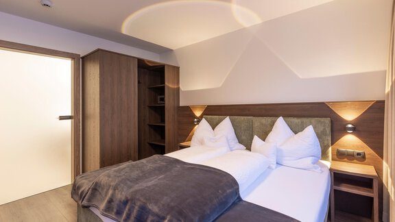 A modern bedroom with two single beds and a cozy bedspread. The walls are painted in neutral colors, and there is a wardrobe as well as bedside tables. - Home4You - Sölden