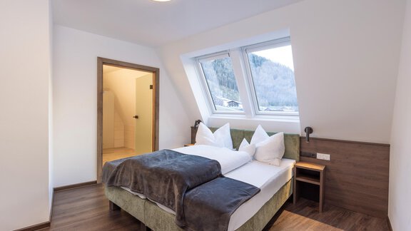 A modern bedroom with a comfortable bed and large windows. The room is bright and welcoming, with a wooden floor and simple furniture. - Home4You - Sölden