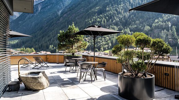 A beautiful terrace with modern furniture and sun umbrellas. In the background, impressive mountains and a clear sky can be seen. - Hotel Alpina - Sölden