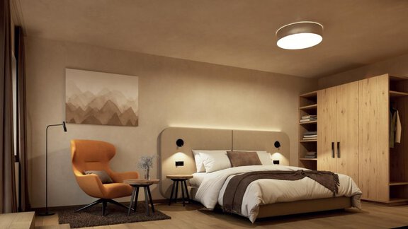 A modern bedroom with a large bed, a cozy armchair, and a wardrobe. The walls are in neutral colors, and a piece of artwork adorns the wall. - Hotel Garni Hainbacherhof - Sölden