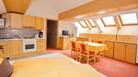 A cozy room with a double bed, a kitchenette, and a dining table. Large windows provide plenty of daylight and a pleasant atmosphere. - Hotel Garni Hainbacherhof - Sölden