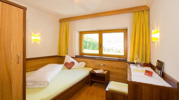 A cozy bedroom with a single bed and wooden furniture. Large windows let in plenty of light and offer a view of the surroundings. - Hotel Garni Hainbacherhof - Sölden