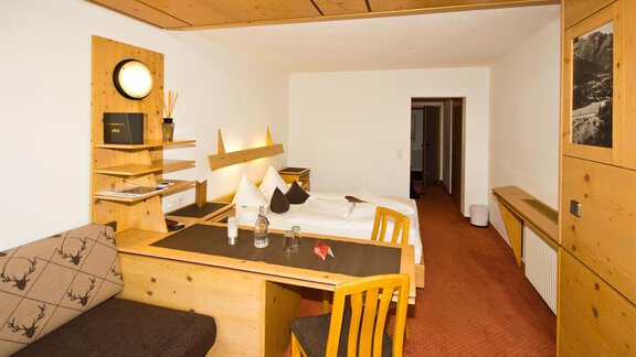 A cozy room with wooden decor and a single bed. A table with chairs and a sofa create an inviting atmosphere. - Hotel Garni Hainbacherhof - Sölden