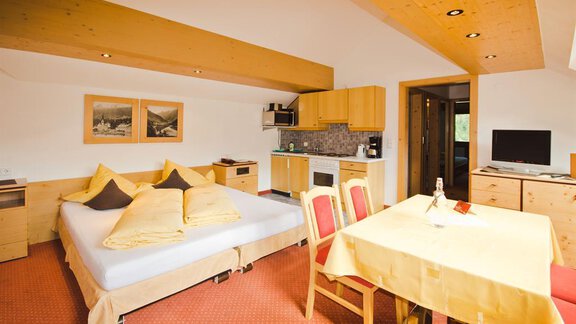 A cozy room with a double bed, a small kitchenette, and a dining area. The wooden elements and warm colors create an inviting atmosphere. - Hotel Garni Hainbacherhof - Sölden