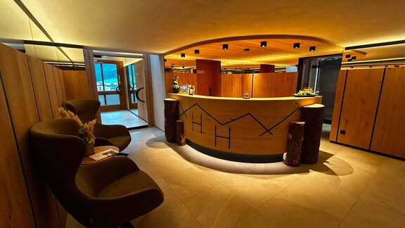 A modern reception area with a round wooden counter. Cozy seating and indirect lighting create an inviting atmosphere. - Hotel Garni Hainbacherhof - Sölden