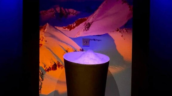A modern room with a round, black pedestal. In the background, snowy mountains and a moody blue lighting can be seen. - Hotel Garni Hainbacherhof - Sölden