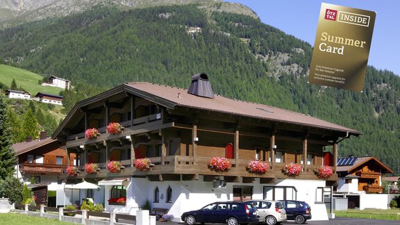 A charming building in the Alps with blossoming flowers on the balcony. In the background, green mountains and a blue sky are visible. - Hotel Garni Maria Theresia - Sölden