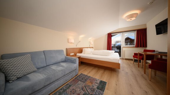 A modern room with a comfortable sofa and a double bed. There is a table with chairs and a window that lets in plenty of daylight. - Hotel Garni Maria Theresia - Sölden