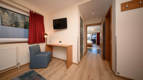 A cozy room with a blue chair, a table, and a TV on the wall. In the background, doors to other rooms are visible. - Hotel Garni Maria Theresia - Sölden