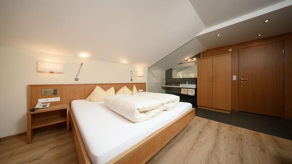 A modern bedroom with a large double bed and wooden paneling. The walls are light, and the room feels cozy and inviting. - Hotel Garni Maria Theresia - Sölden
