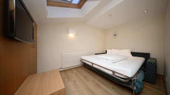 A modern room with a bed and a television. The skylight provides a lot of daylight. - Hotel Garni Maria Theresia - Sölden