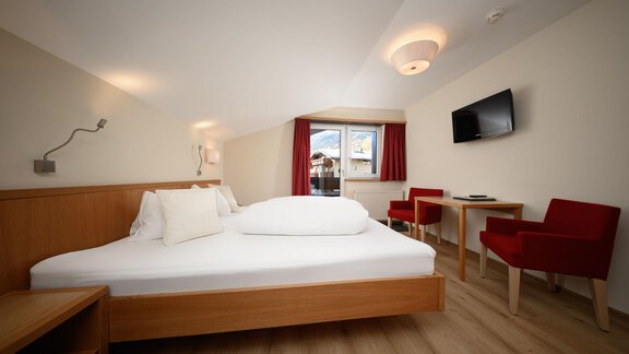 A modern bedroom with a double bed and a cozy table. Red chairs and a flat-screen TV complement the decor. - Hotel Garni Maria Theresia - Sölden