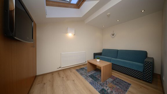 A cozy room with a blue sofa and a wooden table. The skylight provides plenty of daylight. - Hotel Garni Maria Theresia - Sölden
